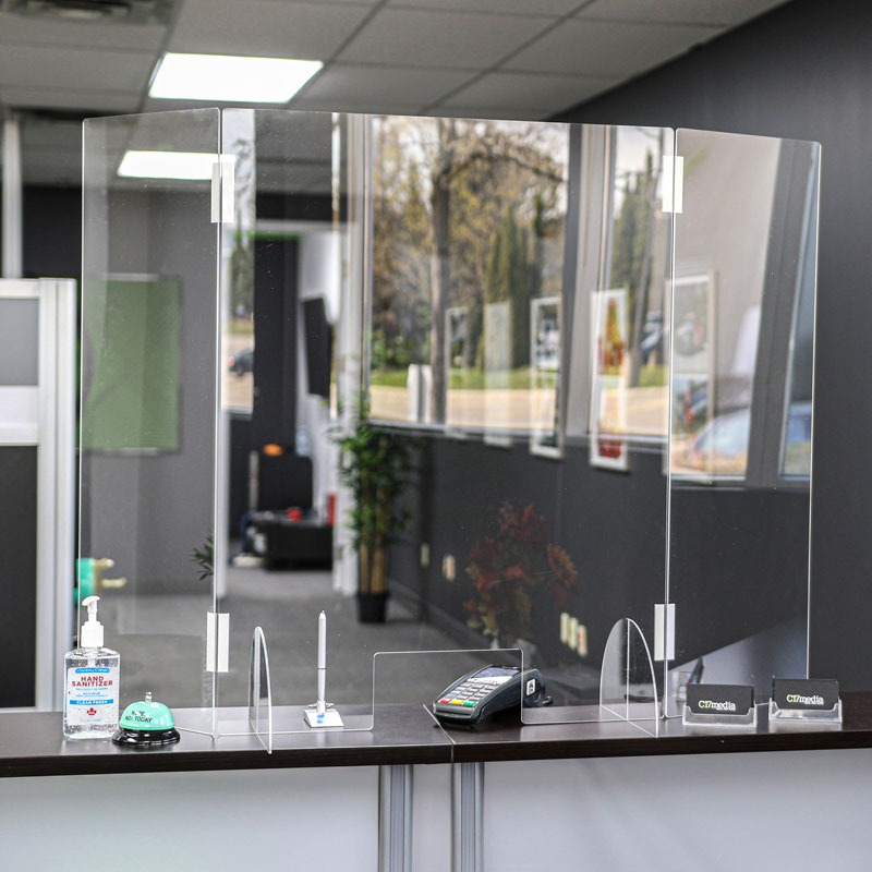 Acrylic sneeze guard at reception desk with hand sanitizer, pen, and payment terminal, illustrating C17media's commitment to safety during COVID-19.