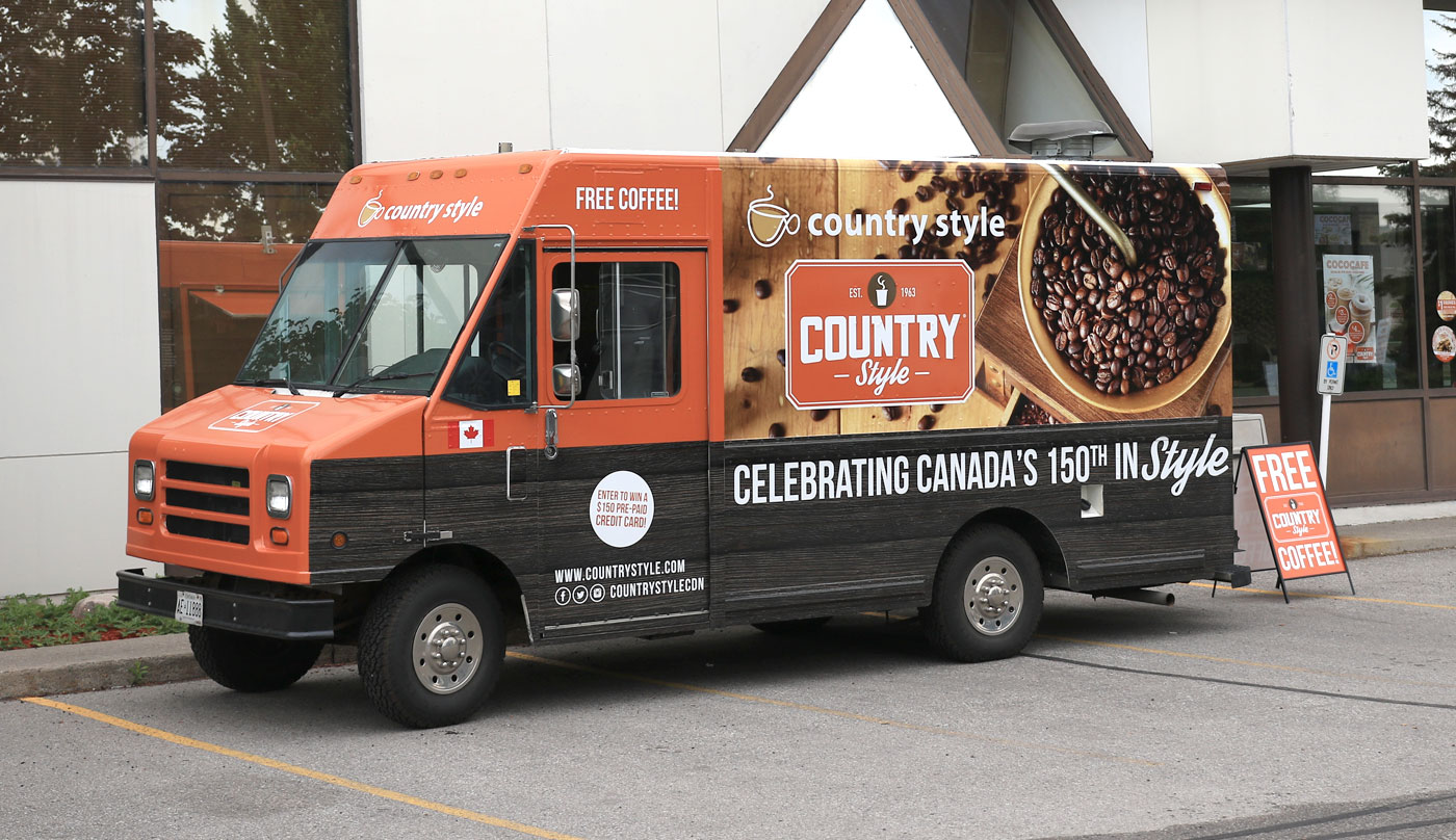 Country Style coffee truck featuring promotional branding, offering free coffee, celebrating Canada's 150th, parked outside a building.