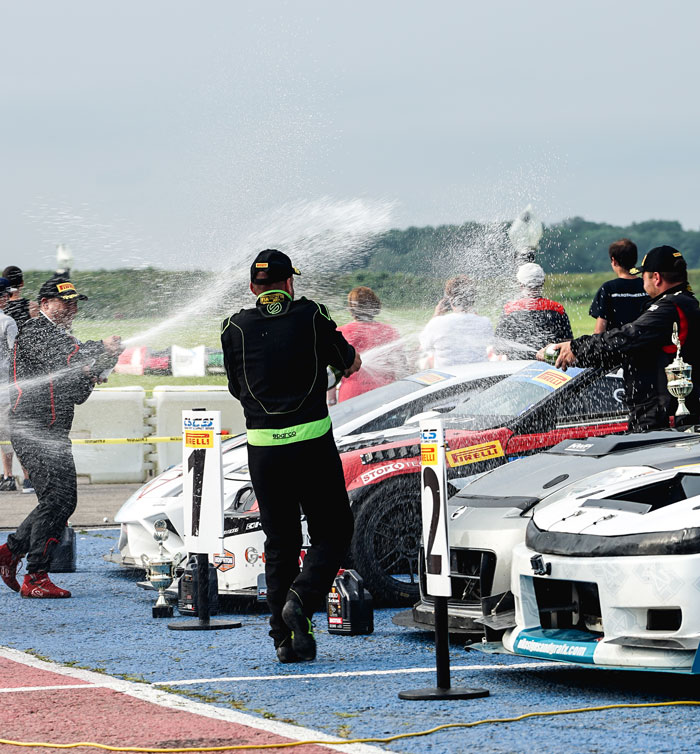 Celebratory scene at CSCS event with drivers spraying champagne beside race cars, showcasing team spirit and post-race festivities.