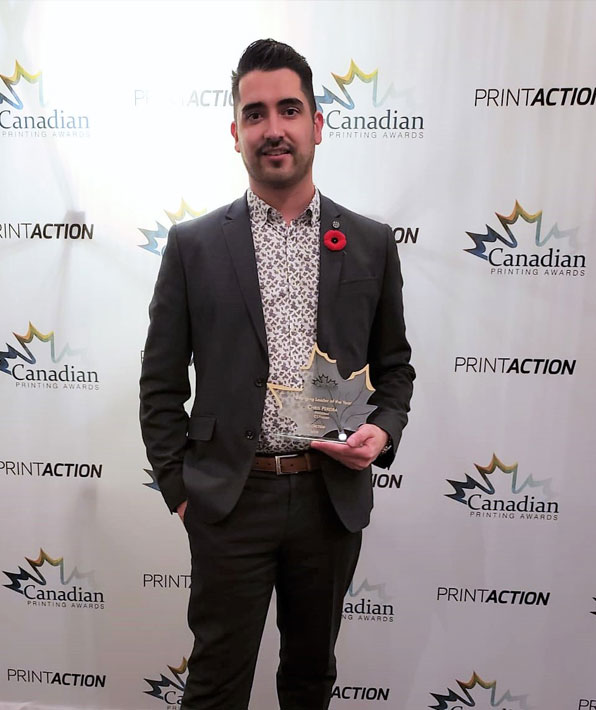 Chris Pereira holding the Emerging Leader of the Year award at the Canadian Printing Awards, with a backdrop featuring PrintAction branding and logos.