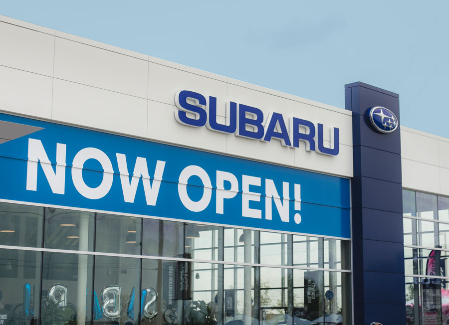 Subaru dealership exterior with prominent "NOW OPEN!" sign, showcasing branding for Pfaff Subaru Guelph and inviting customer engagement.