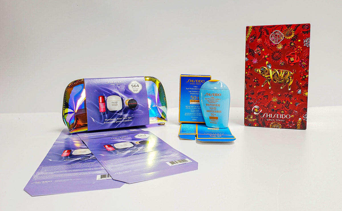 Assorted Shiseido product packaging including an illuminated skin set bag, sunscreen lotion, and promotional materials, showcasing elegant design and premium branding elements.