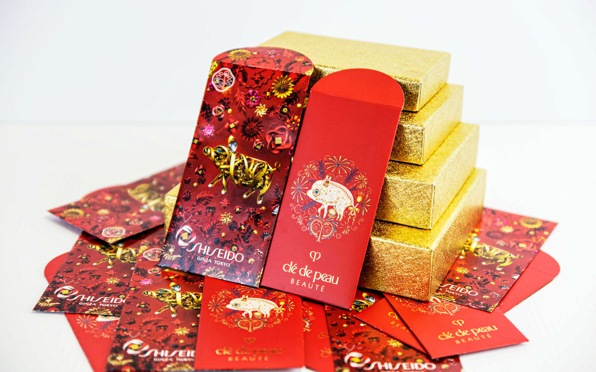 Red and gold packaging designs for Shiseido and Clé de Peau Beauté, featuring intricate illustrations and logos, arranged around golden gift boxes, emphasizing luxury and premium branding.