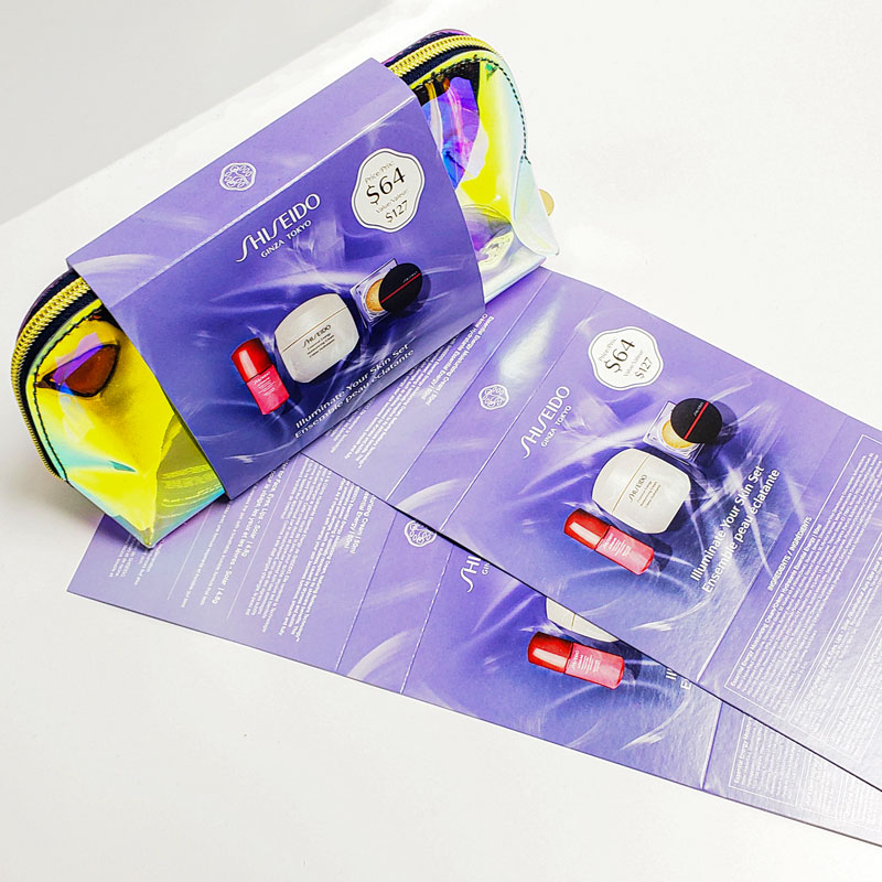 Shiseido product packaging featuring a holographic pouch and promotional cards, showcasing skincare items and pricing details, emphasizing premium brand image and design quality.