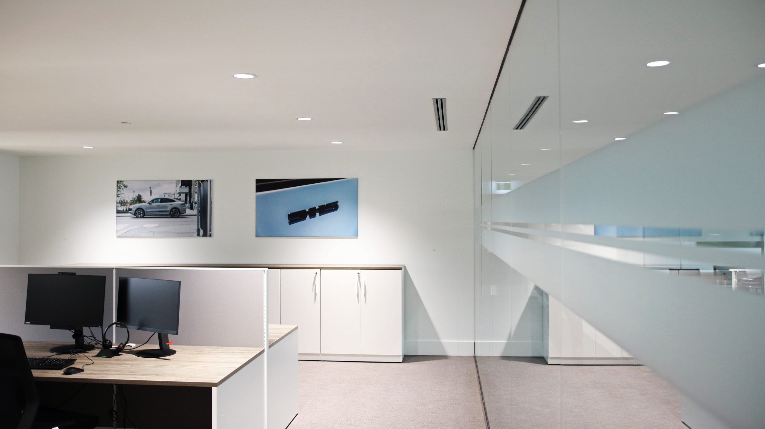Interior office space at Porsche Centre Markham featuring wall-mounted automotive prints, modern workstations with computers, and glass partitions, emphasizing dealership branding and customer experience.