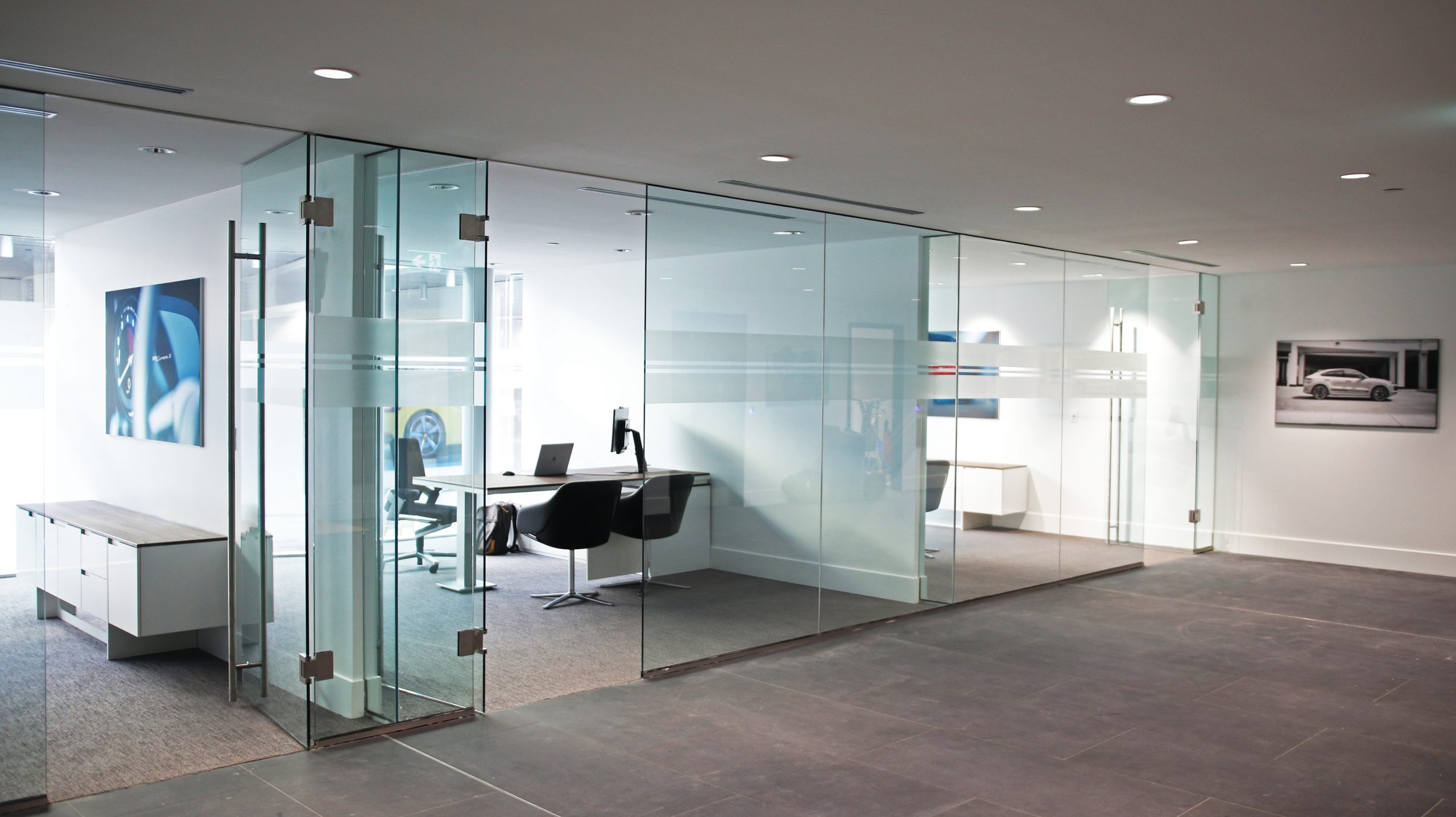 Interior of Porsche Centre Markham featuring glass-walled offices, modern furniture, and automotive artwork, showcasing dealership branding and design elements.
