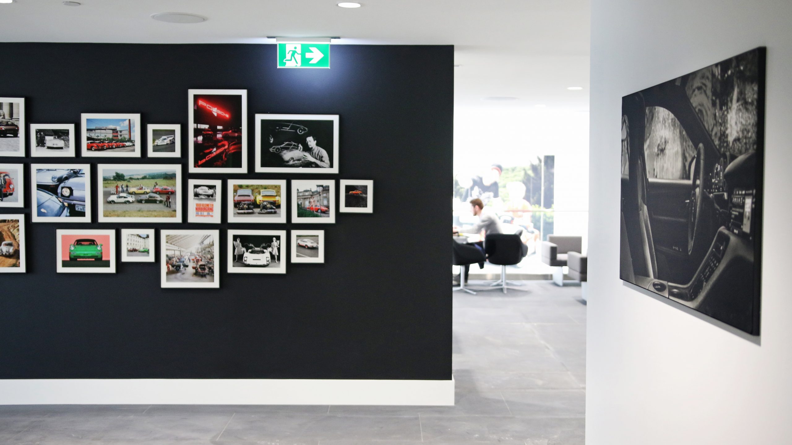 Gallery wall displaying framed photographs of Porsche vehicles and motorsport scenes, enhancing the visual branding of Porsche Centre Markham, with a glimpse of the dealership's interior in the background.