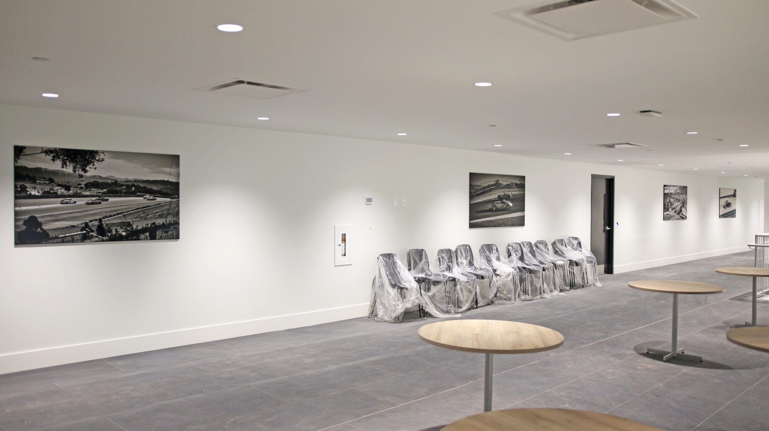 Black and white photographs of racing scenes displayed on walls in an employee area, with plastic-covered chairs and modern tables in a well-lit space.