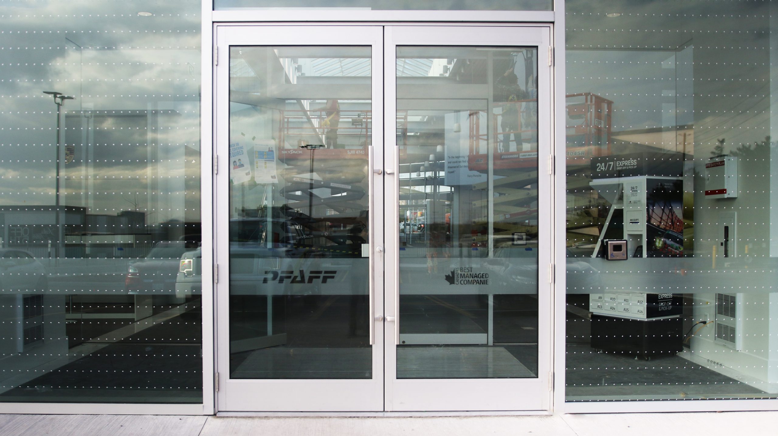 Entrance doors of Porsche Centre Markham featuring PFAFF branding and vinyl frosting, with reflections of the dealership's interior and external signage.