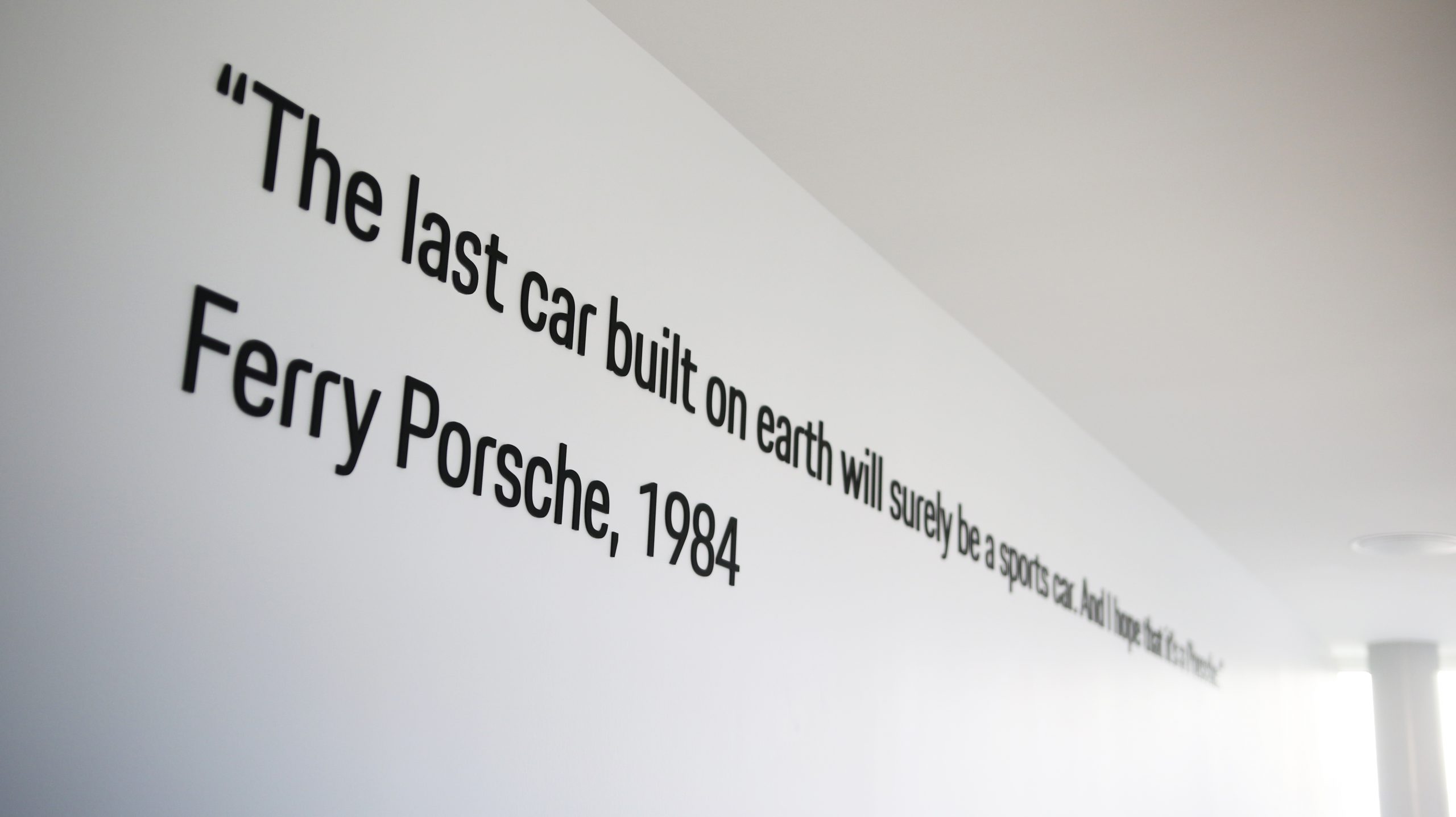 Inspirational quote from Ferry Porsche on a white wall, emphasizing Porsche branding in a dealership setting.