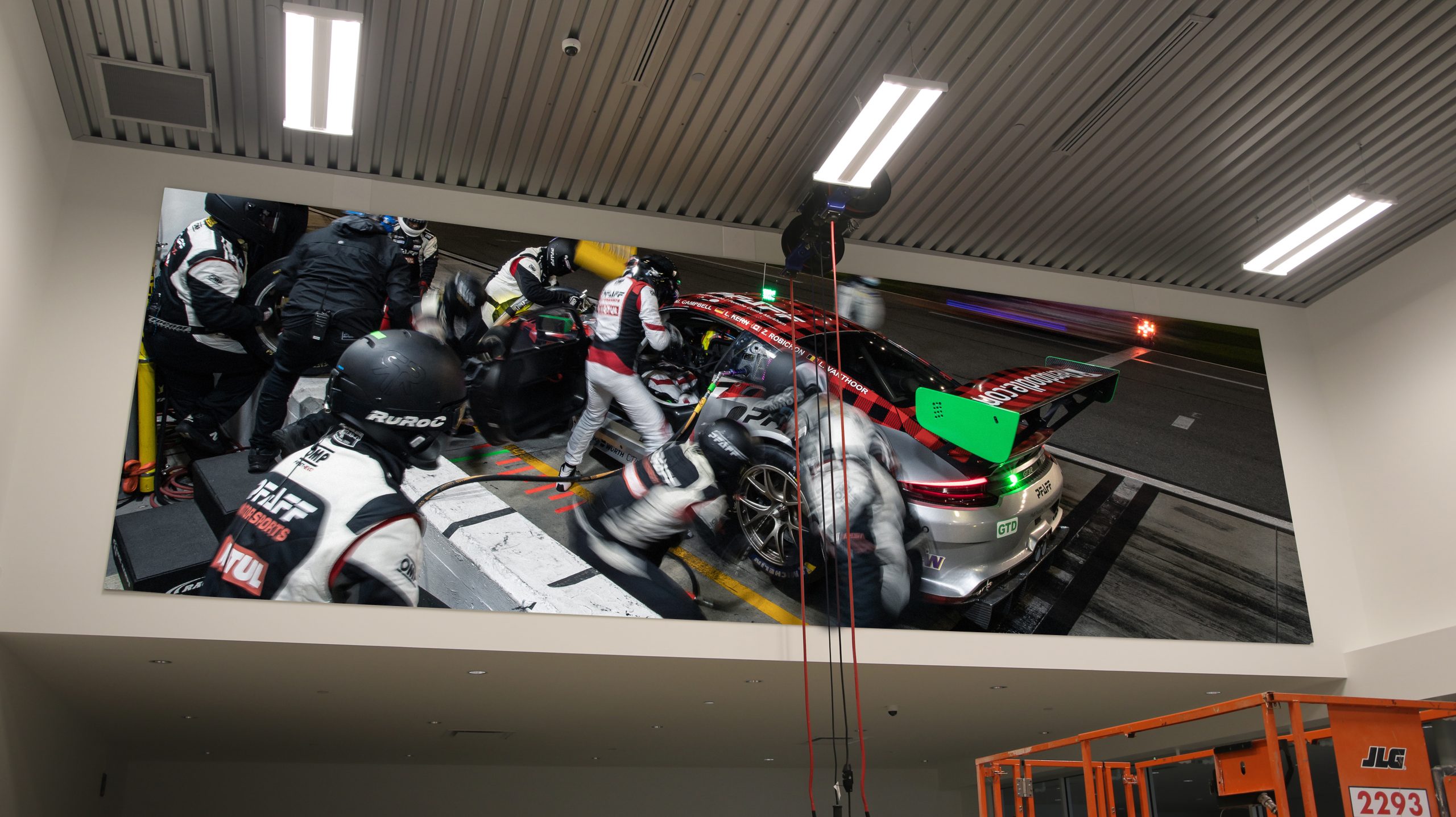 Motorsports-inspired fabric frame showcasing a Porsche GT3 R during a pit stop, with team members in action, enhancing the service area at Porsche Centre Markham.