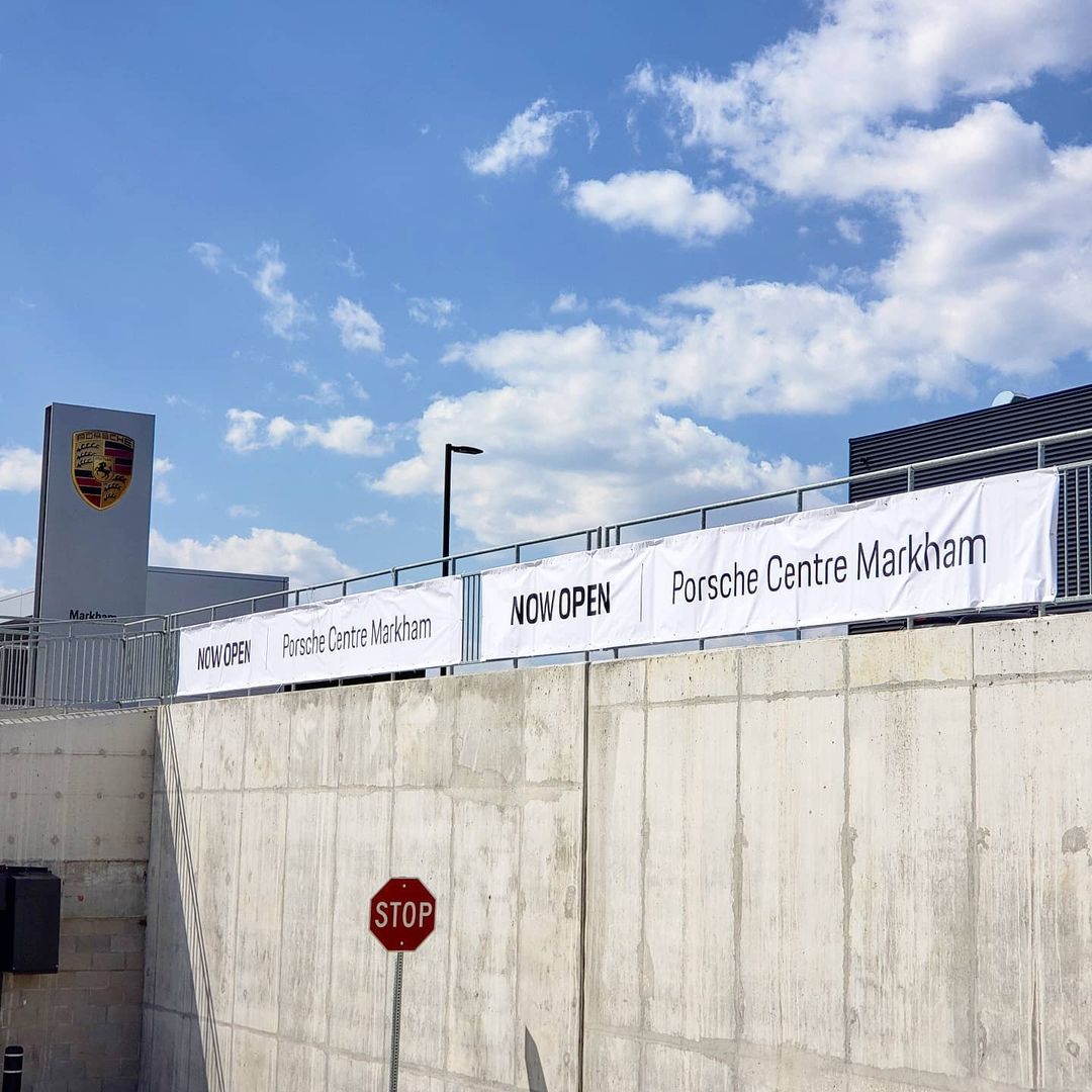 Banners announcing "NOW OPEN" for Porsche Centre Markham, showcasing large format printing on durable materials against a clear blue sky.